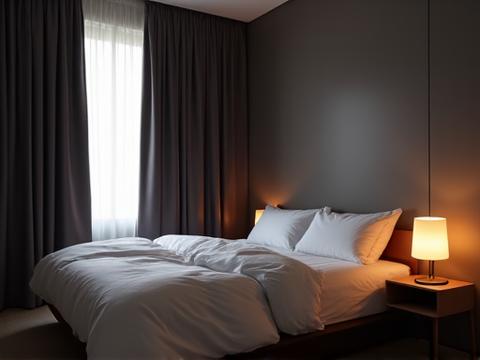 A dark, clean, and minimalist bedroom with blackout curtains, a new comfortable mattress, and soft, warm lighting, representing an ideal sleep environment.